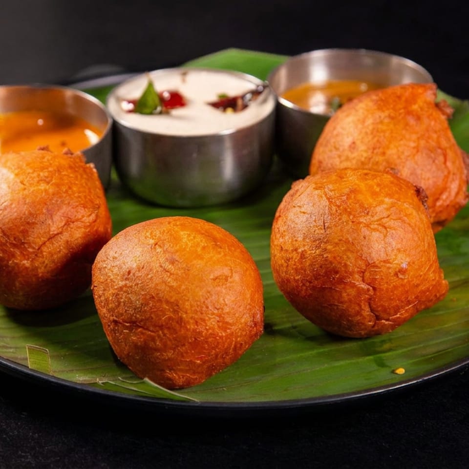 Five golden fried Indian snacks served on a banana leaf with three small bowls of orange curry and creamy sauce.